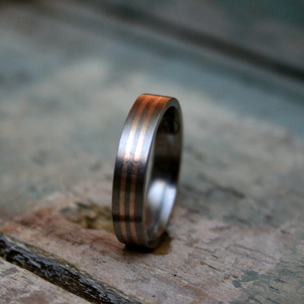 4mm Titanium flat top band with 2 0.5mm 9ct rose gold inlays. The ring is made with a matt finish and a comfort fit on the inside.  As a 4mm band this ring design can work well for both the ladies and the gents.
