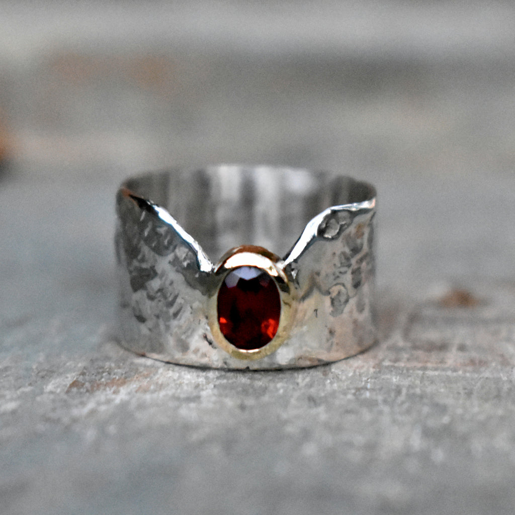Hammered textured sterling silver band with a V-shape cut-in and a 7mm x 5mm oval Garnet set in a 9ct yellow gold tube. The ring is 12mm  in width.  Please note that all pieces are created on order by Erfdeel Juwele. Allow 2 weeks for manufacture.
