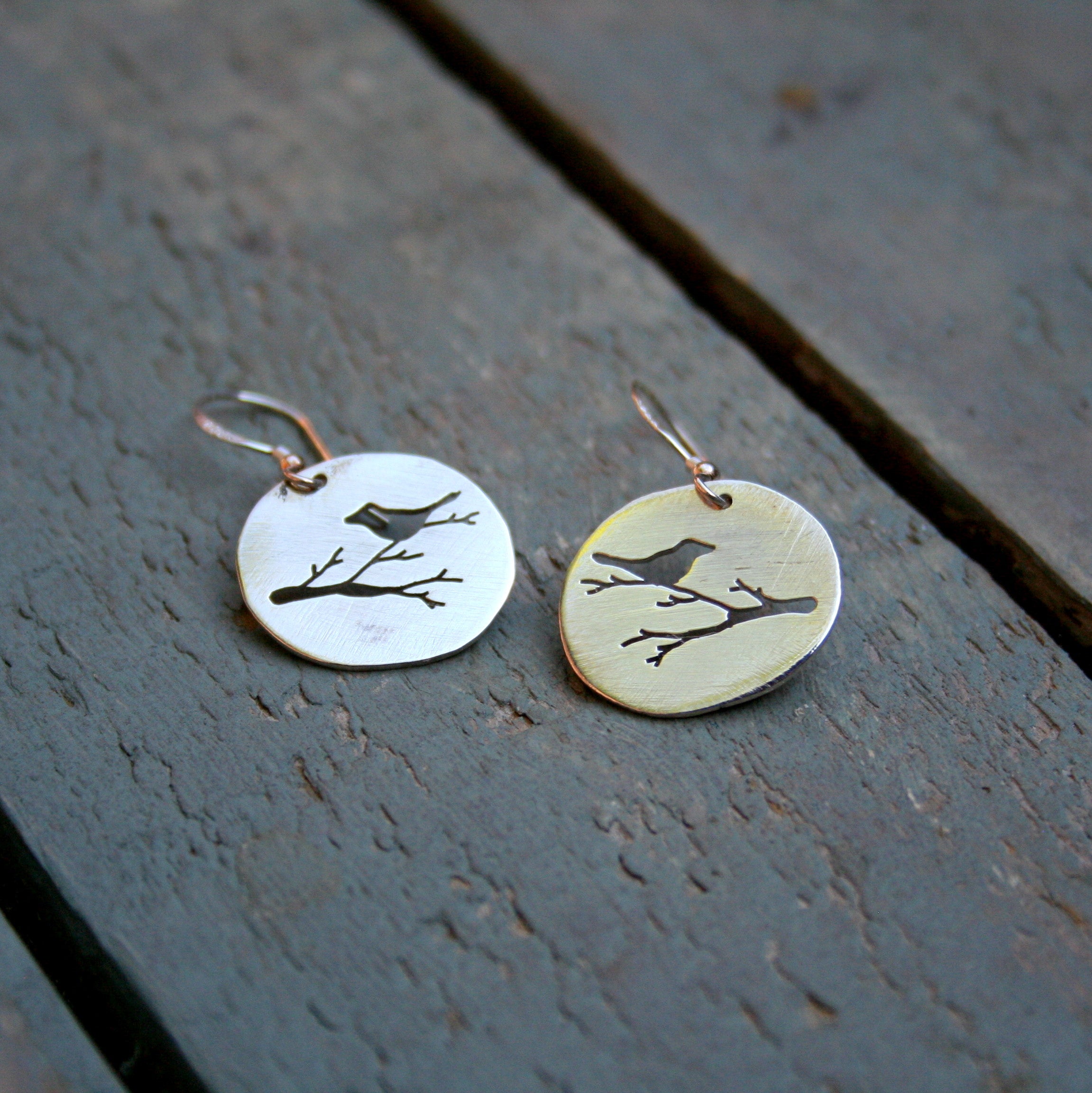 Bird on a branch silhouette hand pierced in an oval sterling silver disc on sterling silver shepherd hooks.  Please note that all pieces are handmade by Erfdeel Juwele on order. Allow up to two weeks for manufacture.