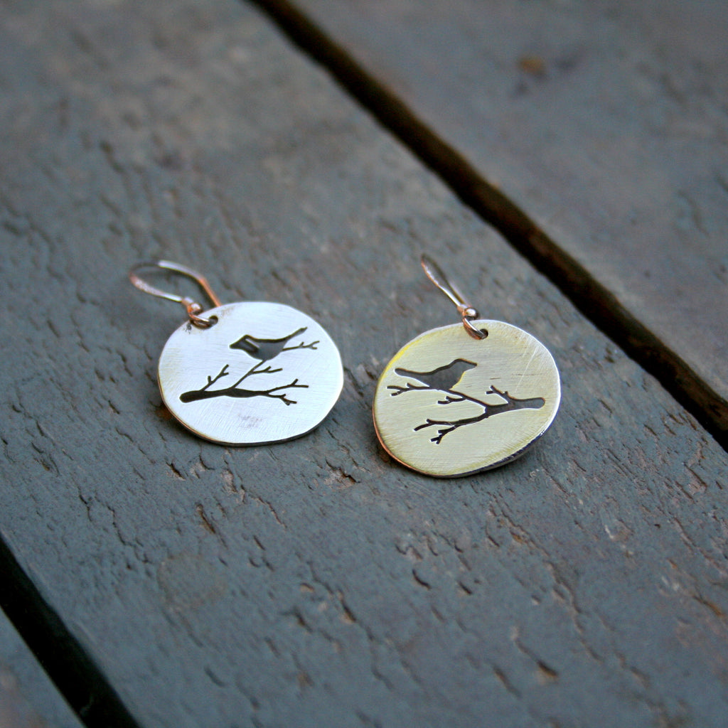 Bird on a branch silhouette hand pierced in an oval sterling silver disc on sterling silver shepherd hooks.  Please note that all pieces are handmade by Erfdeel Juwele on order. Allow up to two weeks for manufacture.