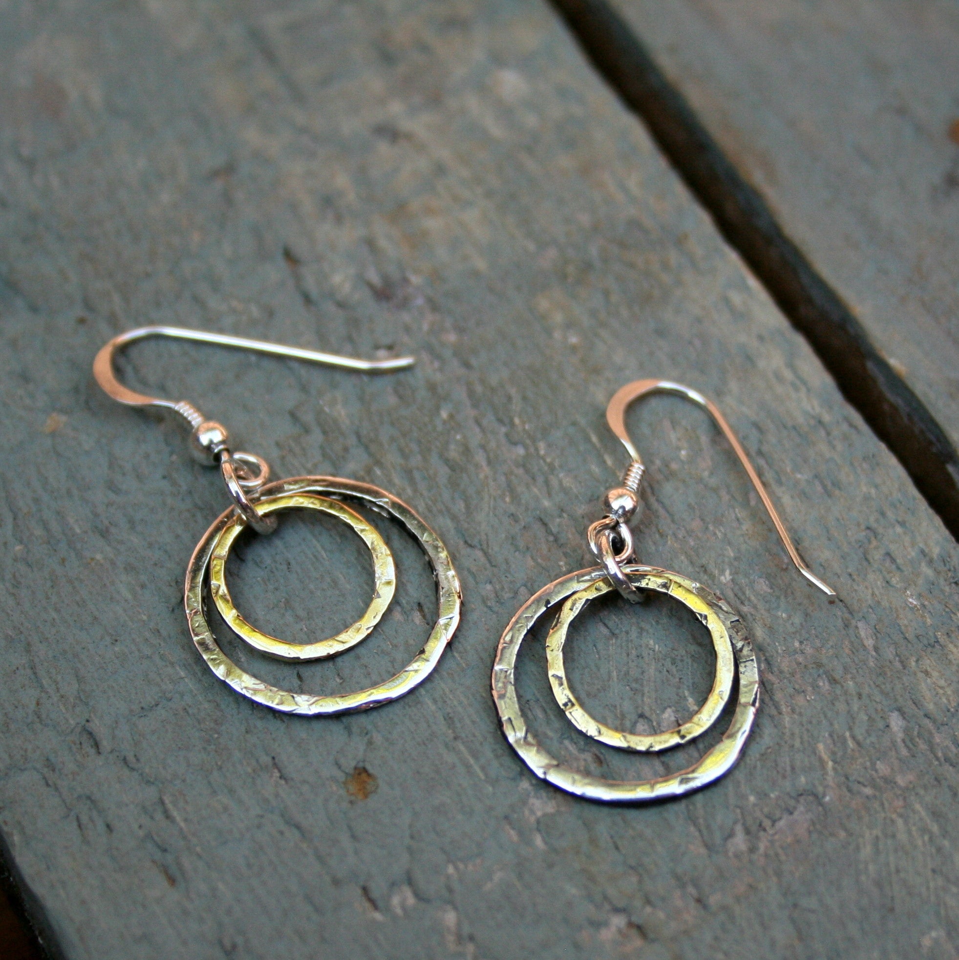 A 13mm brass circle and a 20mm sterling silver circle, both with a hammered textured finish, on a sterling silver hook.  Please note all pieces are handmade on order by Erfdeel Juwele. Allow up to two weeks for manufacture.
